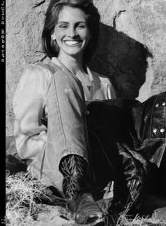 a black and white photo of a woman sitting in front of a rock wall smiling