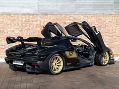 a black and gold sports car parked in front of a brick wall with its doors open