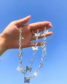 a person's hand holding a chain with butterfly charms on it against a blue sky