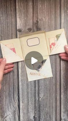 two hands holding an open envelope on top of a wooden surface with the inside flap opened