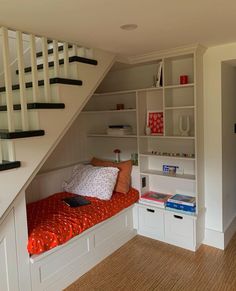 there is a small bed under the stairs in this room with bookshelves and drawers