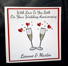 a wedding card with two champagne flutes and hearts on the bottom, which reads, with love to you both on your wedding anniversary