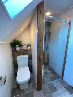 a bathroom with a toilet, shower and tiled flooring in the attic style room