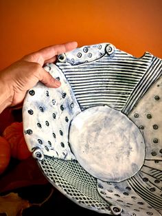 a hand is holding a decorative plate in front of an orange wall