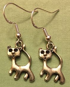 a pair of silver colored cat earrings on a green cloth with metal hooks and earwires