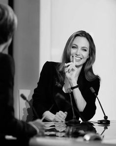 a black and white photo of a woman sitting at a table with a microphone in front of her