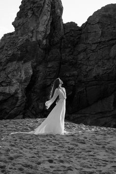 a woman standing on top of a sandy beach next to a rocky cliff and ocean