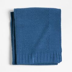 a blue knitted blanket folded on top of a white surface with no one around it