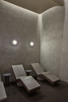 three white lounge chairs sitting next to each other in a room with two round lights on the ceiling