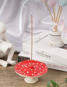 a red and white polka dot plate with sticks sticking out of it next to some books