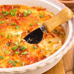 a casserole dish with green onions and cheese in it on a wooden table