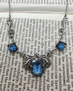 Gorgeous vintage Art Deco necklace with open back blue glass set in chrome filigree. The blue glass is a vibrant sapphire colour and the setting reminds me of a butterfly, which I think is uniquely lovely. There is also a mark on the clasp ring but I can't make it out. In very good vintage condition with some wear to the chrome finish (please see photos), and could use a thorough clean by someone who knows what they're doing. The necklace is 41cm long and the centre stone measures 1.1cm by 0.9cm Victorian Blue Gemstone Necklace, Blue Victorian Jewelry For Collectible, Victorian Blue Jewelry For Collectors, Antique Blue Gemstone Necklaces, Blue Art Deco Jewelry For Party, Ornate Blue Necklace With Intricate Design, Ornate Blue Nickel-free Jewelry, Vintage Blue Jeweled Necklaces, Ornate Nickel-free Blue Jewelry