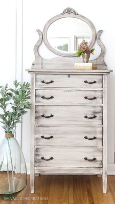 an old dresser with a mirror and vase on it next to a plant in a glass vase