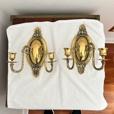 two gold wall sconces on a white cloth with candles in front of them