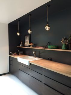 a kitchen with two sinks and hanging lights over it's counter top, in front of a black wall