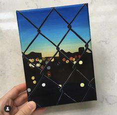 a hand holding up a piece of art that looks like a fence with lights on it