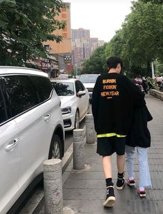 two people walking down the sidewalk next to parked cars