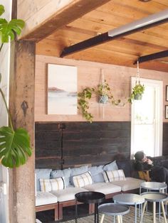 a living room filled with lots of furniture next to a wooden wall covered in plants