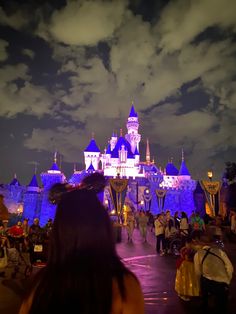 people standing in front of a castle at night with lights on it and clouds overhead