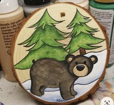 a bear painted on a wood slice with pine trees in the background and other crafting supplies