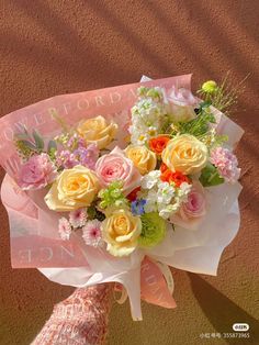 a bouquet of flowers sitting on top of a pink paper wrapped in white and yellow ribbon