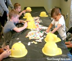 several children sitting at a table with yellow helmets on it and confetti all over the table