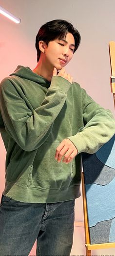 a young man leaning against a chair wearing a green hoodie