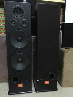 two black speakers sitting next to each other on the floor in front of some boxes