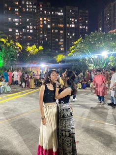 two women standing next to each other in front of tall buildings at night with lights on