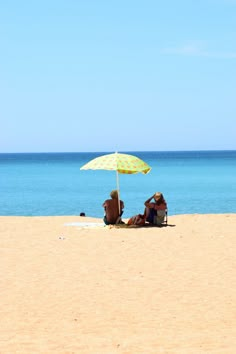 two people sitting under an umbrella on the beach