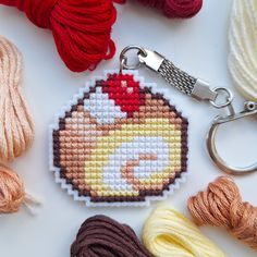 a cross - stitch keychain with some yarn and scissors on top of it