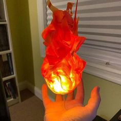 a hand is holding an orange lamp in the shape of a flower with petals on it