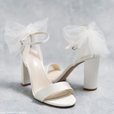 a pair of white high heeled shoes with a bow on the toe and ankle strap