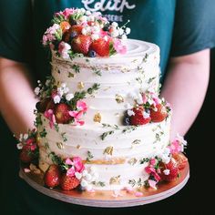 a white cake with strawberries and flowers on top is being held by a person