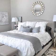 a bedroom with gray walls and white bedding in the center, along with a large round mirror on the wall