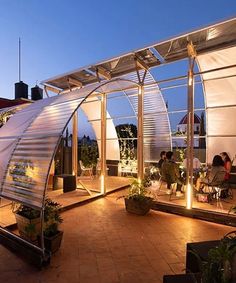 people are sitting outside in the evening on an outdoor patio with glass walls and plants