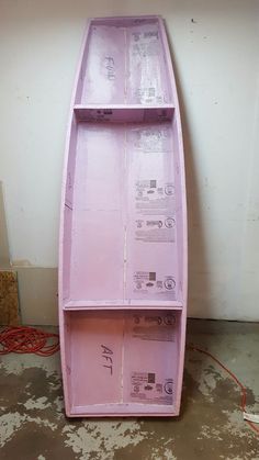 a pink boat shaped shelf sitting on top of a floor next to a white wall