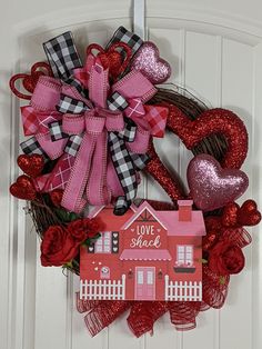 a heart shaped wreath with a house and two hearts hanging from it's front door