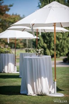 an umbrella and table set up in the grass for a wedding reception with white linens