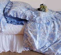 an unmade bed with blue and white bedspread, pillows and flowers on it