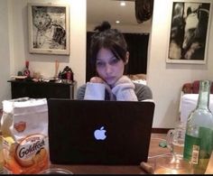 a woman sitting in front of a laptop computer on top of a wooden table next to bottles