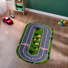 a child's play area with toy cars on the floor and green grass in the shape of a road