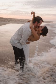 a man and woman standing in the water at the beach with their arms around each other