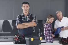 two men and a woman standing in a kitchen with their arms crossed, looking at the camera