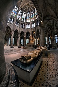 the interior of a cathedral with stained glass windows and stone benches in front of them