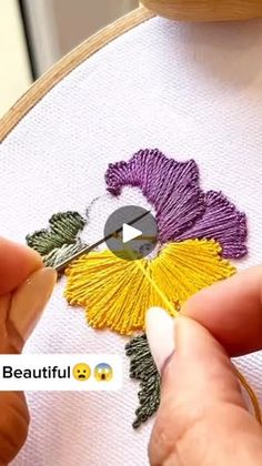 someone is stitching a flower with yellow and purple thread on the back of a cross - stitch