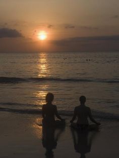 two people sitting on the beach at sunset