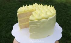 a white cake with yellow frosting sitting on top of a wooden table in the grass