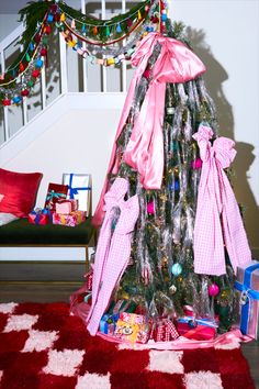 a decorated christmas tree with pink bows and presents on the floor next to it in front of stairs