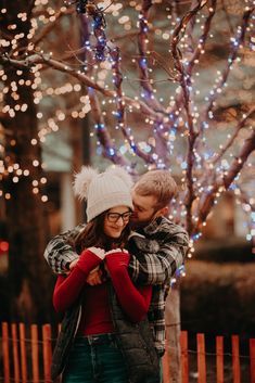 a man and woman hugging in front of a tree with christmas lights on the branches